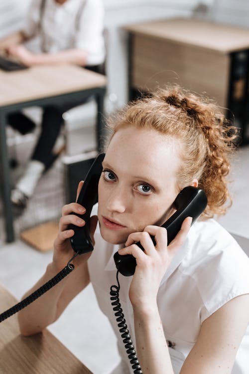 Free Focused young woman multitasking with phones in a professional office setting. Stock Photo